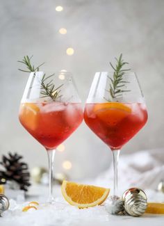 two glasses filled with red wine and garnished with rosemary sprigs next to christmas decorations