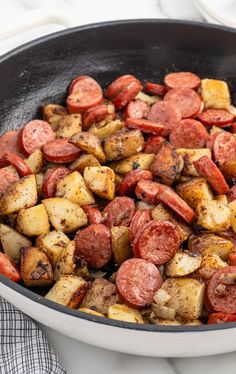 cooked sausage and potatoes in a skillet on a marble counter top with a towel