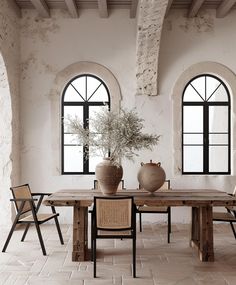 a table with chairs and vases on it in front of two arched windowed windows