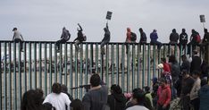 a group of people standing on top of a metal fence next to the ocean while holding signs