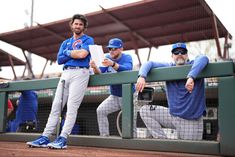 three baseball players sitting on the dugout with their arms crossed and looking at something