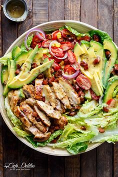 a salad with chicken, lettuce, tomatoes and avocado on top