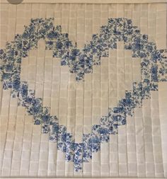 an embroidered heart is displayed on a piece of white fabric with blue flowers in the center