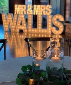 two candles are sitting on a table with greenery and lights in the background that read mr & mrs walies