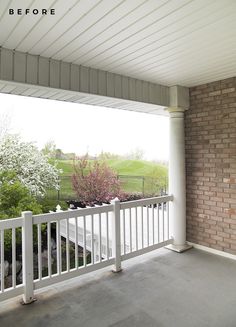 an empty balcony with white railings and brick walls, overlooking a green field in the distance