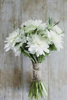 a bouquet of white flowers is tied to a wooden wall with twine around it