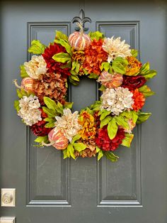 a wreath on the front door with flowers and pumpkins hanging from it's side