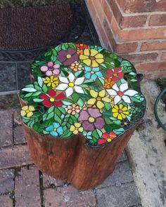 a wooden stump with stained glass flowers on it sitting next to a brick wall and potted planter