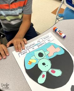 a young boy sitting at a table with a paper cut out of a teddy bear