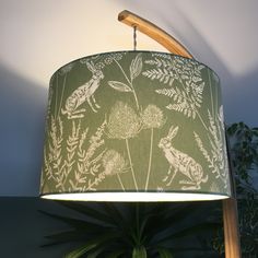 a green lamp shade with white flowers and leaves on the fabric, hanging from a wooden pole