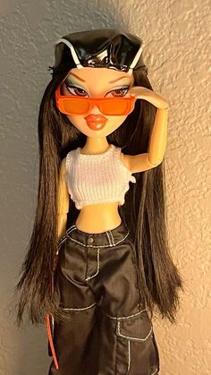 a doll with sunglasses and leather pants is posed for the camera on a white wall