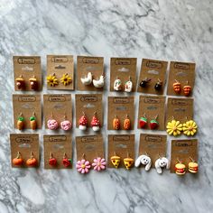 twelve pairs of earrings are displayed on a marble counter top, each with different designs and colors