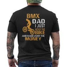 a man wearing a t - shirt that says bmx dad i just hold the bike and hand over the money