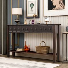 a console table with drawers and baskets on it in a room decorated with pictures, lamps, and paintings