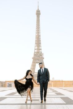 a man and woman standing in front of the eiffel tower, holding hands