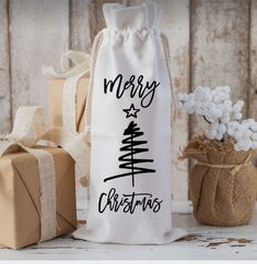 a white bag with merry christmas written on it next to two wrapped presents and a small potted plant