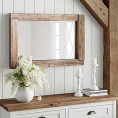 a white vase with flowers on top of a wooden table in front of a mirror