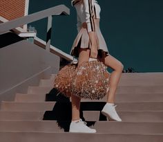 a woman is walking down some stairs with a handbag on her shoulder and white sneakers