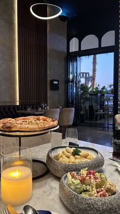 two pizzas are sitting on the table in front of some drinks and plates with food