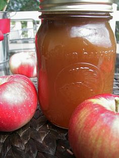 two apples sitting on top of a table next to a jar of apple cider