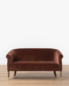 a brown velvet couch sitting on top of a wooden floor next to a white wall