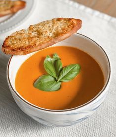 there is a bowl of soup with bread on the side and garnished with basil