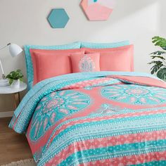 a bed covered in pink and blue comforter next to a potted green plant