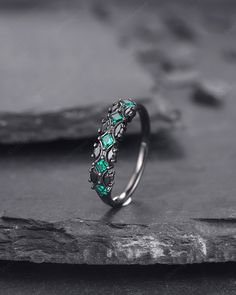 a silver ring with green stones on it sitting on top of a stone slab in front of