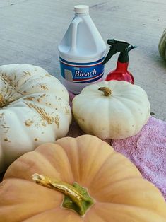 several pumpkins and cleaning products are on the ground next to each other, including a bottle of bleach