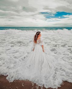 a woman in a white dress standing on top of a beach next to the ocean