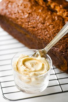 a loaf of bread sitting on top of a cooling rack next to a bowl of whipped cream