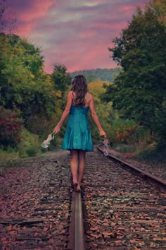 a woman walking down the train tracks with her hands in her pockets and holding flowers