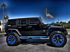 a black jeep with blue rims parked in a parking lot next to an american flag