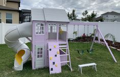 a purple play set with a slide and climbing frame in the grass next to a white fence