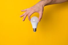 a person's hand reaching out to an electric light bulb on a yellow background