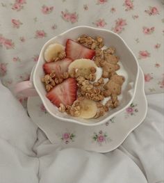 a bowl filled with granola and fruit on top of a floral cloth covered bed