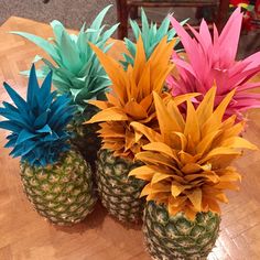 three pineapples with colorful paper flowers in them sitting on a wooden table top