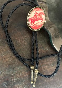 This awesome bolo tie has a vintage cowboy print with a clear resin coating and metal backing. Handmade in our shop! The cord is black and genuine leather. Our bolos pair nicely with many of our belt buckles! They make wonderful gifts. The western bolo tie rope length is 39' ; pendant size is 1 1/2'' x 1 1/4'' Vintage Adjustable Bolo Ties, Vintage Black Bolo Ties For Gift, Vintage Black Bolo Ties As Gift, Vintage Black Jewelry For Western-themed Events, Adjustable Black Bolo Tie For Rodeo, Black Adjustable Bolo Ties For Rodeo, Adjustable Black Bolo Ties For Rodeo, Handmade Adjustable Bolo Ties For Western-themed Events, Vintage Bolo Tie With Adjustable Length For Western Events