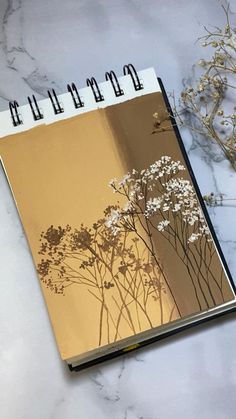 an open spiral notebook sitting on top of a table next to dried flowers and plants