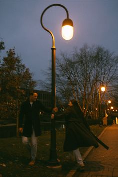 a man and woman holding hands while standing next to a lamp post on a sidewalk