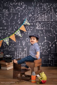 a little boy sitting on top of a wooden chair in front of a chalkboard