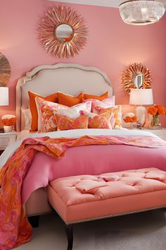 a bedroom decorated in pink and orange with a white headboard, footstool, mirror, and ottoman