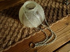 a white vase sitting on top of a wooden table next to a chain link bracelet