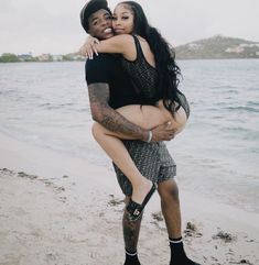 a man holding a woman on the beach with water in the backgrouds