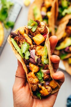 someone holding up a taco filled with meat and vegetables