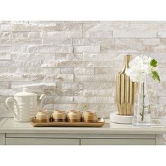 white flowers and vases sit on a table in front of a wall made of stone