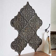 an ornate metal wall hanging on the side of a white wall next to a vase