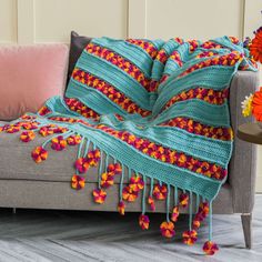 a couch with a colorful blanket on top of it next to a vase filled with flowers