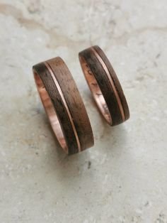 two wedding bands made out of wood and copper are sitting on a marble countertop