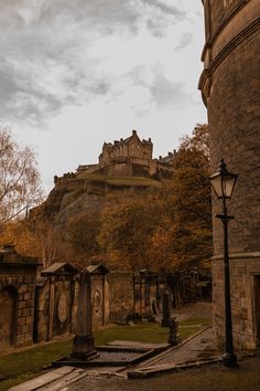 an old castle on top of a hill with trees in the foreground and tombstones below